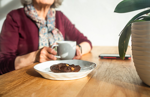 Cropped shot of a senior woman having coffee and chocolate brownie while sitting at table at home