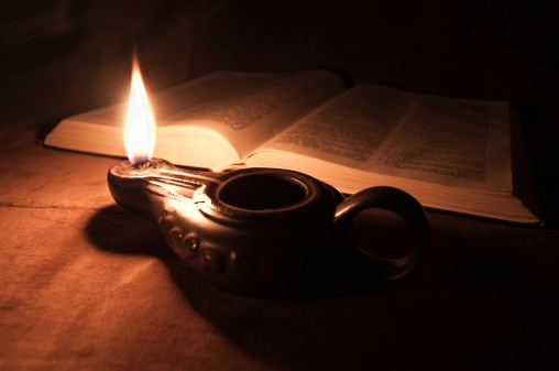 Close-up of an oil lamp and an opened Bible.