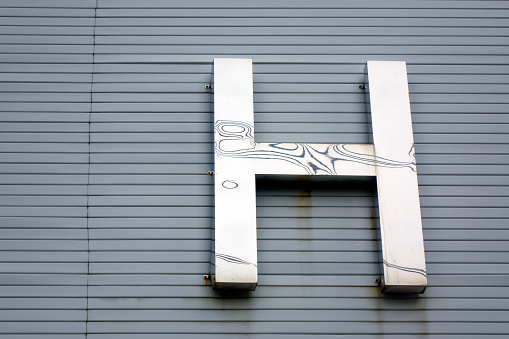 Shiny metalwork letter H on building wall