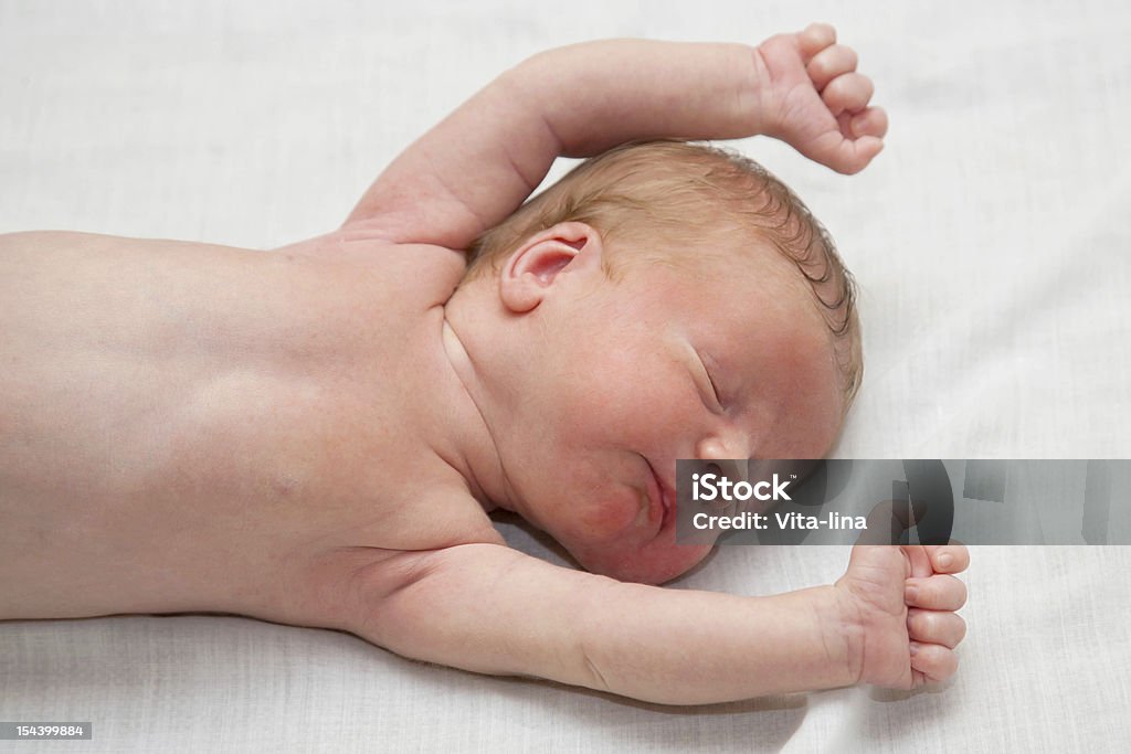 Sleeping newborn Peacefully and soundly sleeping naked newborn tiny slim baby. His hands clenched into fists. He sleeps on the white sheet. Bed - Furniture Stock Photo