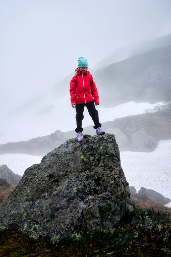 A little girl stands on a volcanic rock in foggy weather