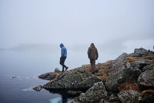 Two tourists approach the lake shore in foggy weather