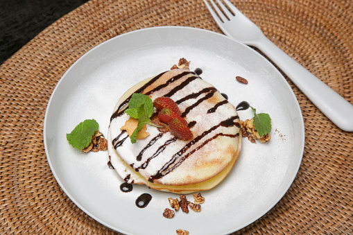 Thick and fluffy American pancakes drenched in chocolate syrup with fresh strawberries and mint leaf