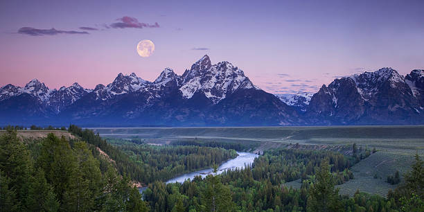Moon setting over the Tetons Panoramic of a full moon setting over the mountains of Grand Teton National Park prior to sunrise, as seen from the Snake River Overlook.  File sizes up to XL available. teton range photos stock pictures, royalty-free photos & images