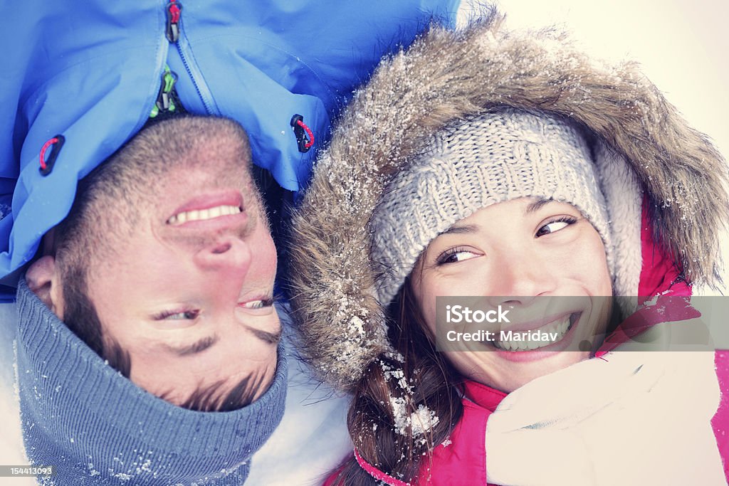 Joyful Asian / Caucasian couple Happy winter couple. Cropped view of the faces of a joyful young interracial Asian / Caucasian couple lying on their backs in snow with their heads close together. 20-29 Years Stock Photo