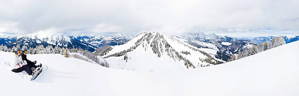 Two snowboarders taking a break and looking at mountain panorama stock photo