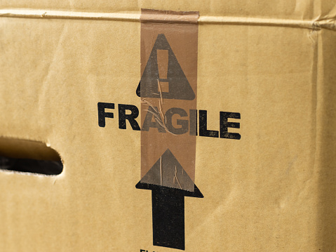 Fragile warning on a parcel and a brown tape on it. Sign to prevent careless handling of the package during shipping. Transportation of goods and products to the customer.