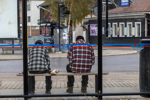 Arjeplog, Sweden June 8, 2023 Two young men sitting at a bus stop wearing similar shirts with a bread baguette between them