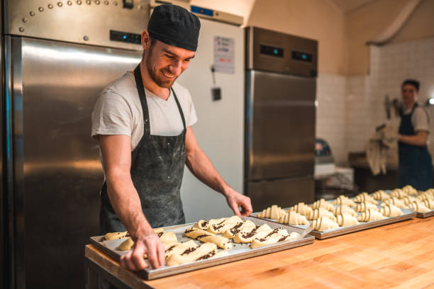 istock Caucasian Artisan Baker Stacking Raw Pastries On A Baking Tray 1544266706