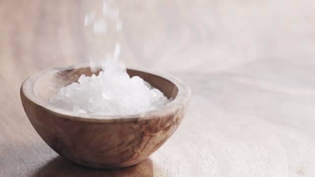 Slow motion of coarse sea salt crystal falling into wood bowl on wooden table