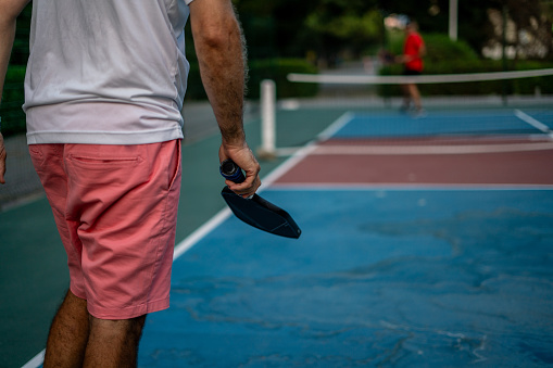 Men is playing pickleball on outdoor hard court ball is on his hand vertical sport close up still