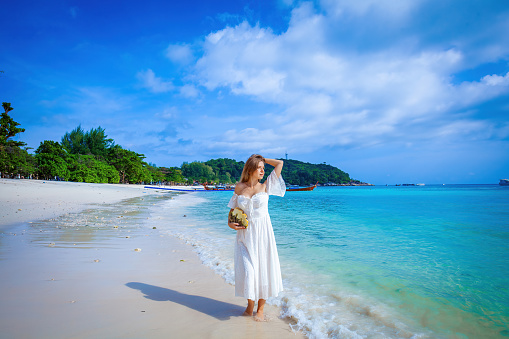 Traveler enjoys the sea and beach. Young woman in white dress with seashell. Concept of vacation and relaxation.