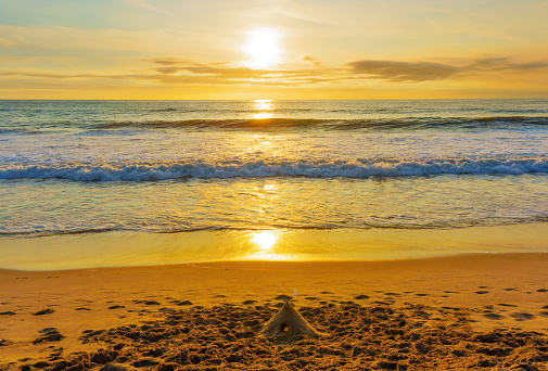 Enchantment of Venice Beach as the sun gracefully sets over the horizon and the golden pathway of light passes the ocean waves and touches a sandcastle on the beach. Inspirational poster background.