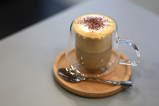 A latte coffee is served in a double-layer glass cup at a café.