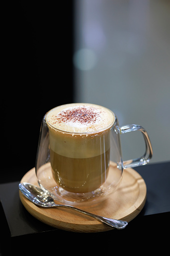 A latte coffee is served in a double-layer glass cup at a café.