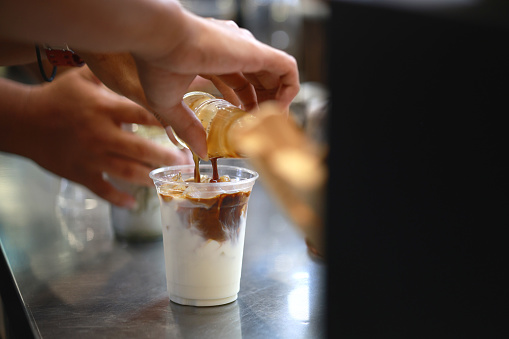 In a close-up shot, a barista's hand skillfully pours espresso over cold milk, creating an ice latte. The careful pour blends the rich espresso with the smooth milk, resulting in a refreshing and delightful beverage.
