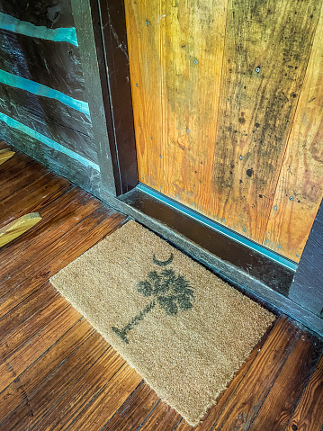 Angled view of a doormat with the South Carolina state logo in front of old cabin door.