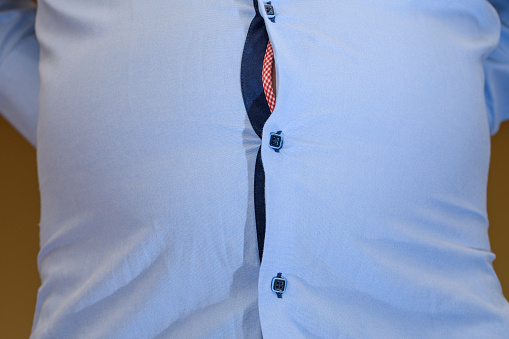 Abdominal bloating, big male belly and tight shirt with taut buttons, macro closeup