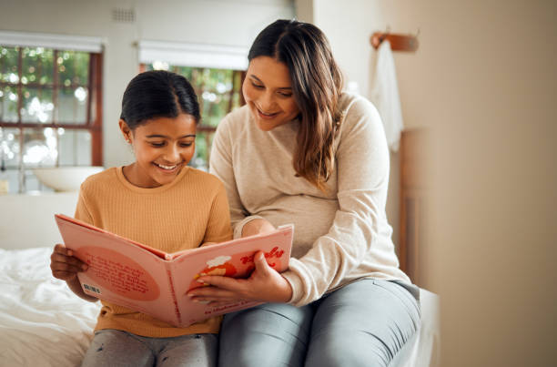istock Pregnant mother reading to kid for fun learning, language and home development help, support and bonding. Family, Indian people or mom and child, storytelling book for creative education or teaching 1545226790