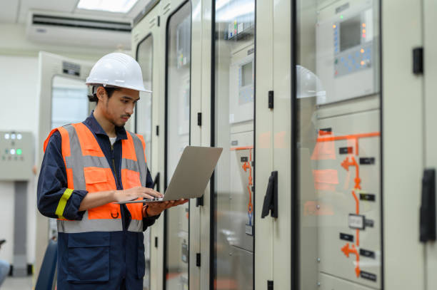 istock Asian electrical technician worker with personal safety equipment using laptop computer operating or check status from control panel switch board in control room of high voltage electric transformer station. Industrial business occupation worker concept. 1545227822
