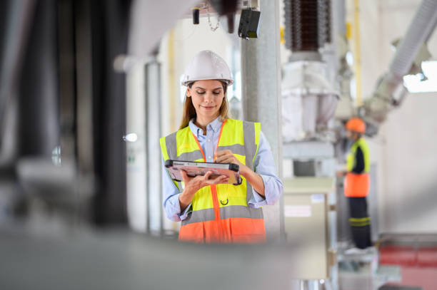 istock Caucasian electrical technician worker woman with personal safety equipment using digital tablet check list operating or check status of high voltage circuit breaker switch of high voltage electric transformer sub station 1545228355