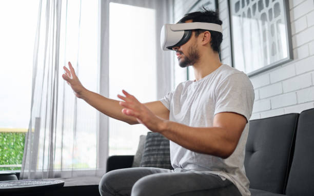 istock Virtual reality, hands and man on sofa with futuristic headset for interactive, online and 3d games ux. Technology, digital tech and male relax with vr glasses for metaverse, cyberspace and gaming 1545237337