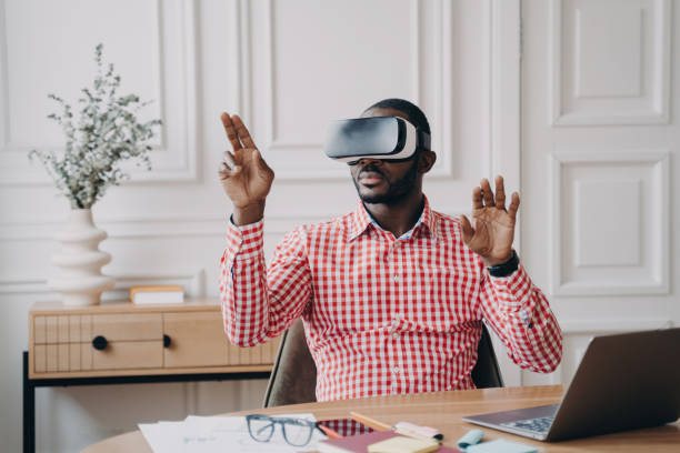 istock Focused Afro American businessman, VR headset on, immersed in virtual reality game; gesturing, interacting with cyber world objects. 1545250698
