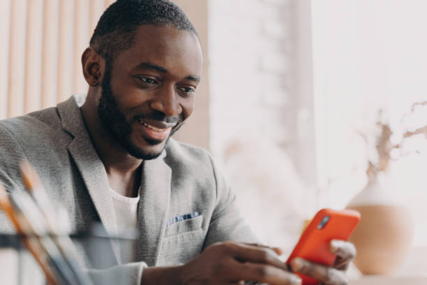 istock Handsome African American businessman, mobile use, chatting online, office desk, typing message, positive smile, distracted from work. 1545250848
