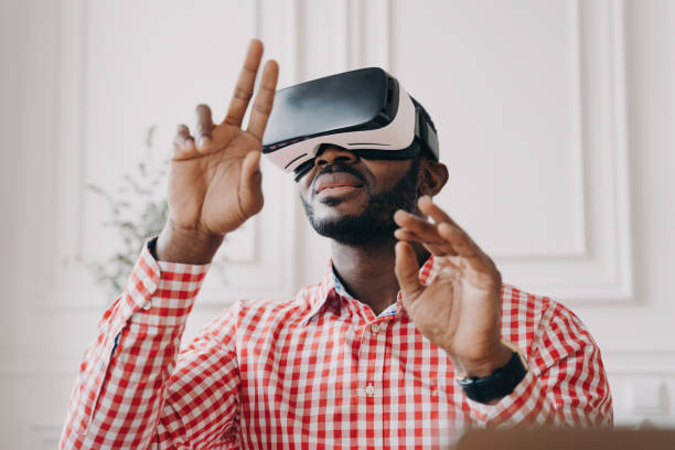istock Excited African male in VR glasses explores augmented reality, waving hands, making touch gestures, against home office backdrop. 1545250951