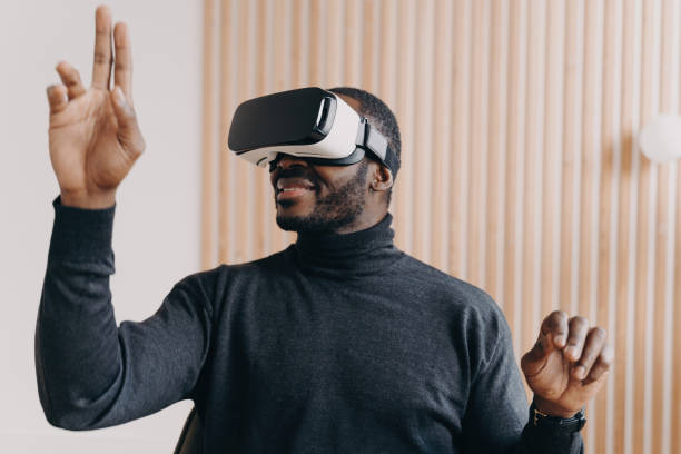 istock Smiling African American businessman in VR glasses, office setting, testing virtual reality goggles, impressed with 3D technology, interacting with virtual objects. 1545251216