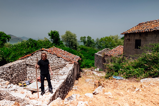 Man in black standing on the ruins of a fishing village stone houses.