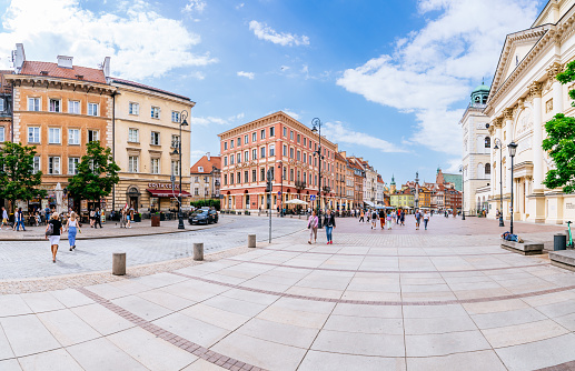 A view of Krakowskie Przedmieście street, a bustling thoroughfare located in Warsaw's Old Town Center (Stare Miasto w Warszawie, Warszawska Starówka). On the right side stands Kościół Akademicki św. Anny (St. Anne's Academic Church), an architectural structure showcasing unique features. On the background, Plac Zamkowy (Castle Square) can be seen, an open space surrounded by historical attractions. The street itself is filled with pedestrians going about their day, and various buildings contribute to the overall urban scenery. This photograph provides a factual representation of Krakowskie Przedmieście street, featuring the notable presence of Kościół Akademicki św. Anny and Plac Zamkowy, within Warsaw's cherished Old Town Center.