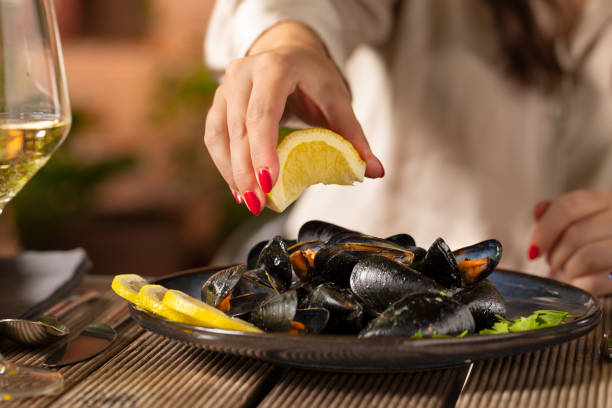 jeune femme versant du jus de citron sur des moules cuites à la vapeur - prepared shellfish seafood crustacean mussel photos et images de collection