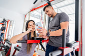 Fitness instructor showing how to do a exercise on mobile phone to young woman in the gym