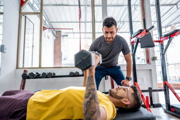 Personal trainer teaching student how to bench press correctly at the gym Personal trainer teaching student how to bench press correctly at the gym chest dumbbells ripl fitness