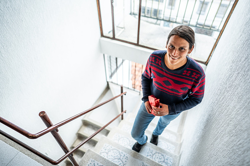 Portrait of a young man walking up stairs holding a gift on a entryway in a building