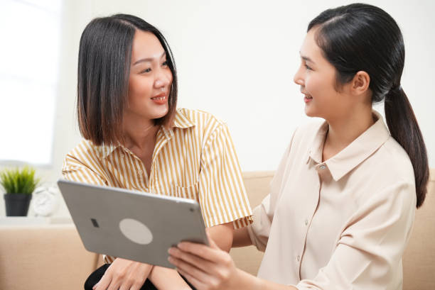 istock Affection LGBT concept. Happy diverse beautiful asian female lesbian couple talking and using tablet in living room spending quality time together, technology and love. 1545346413