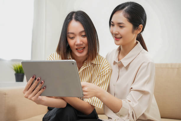 istock Affection LGBT concept. Happy diverse beautiful asian female lesbian couple talking and using tablet in living room spending quality time together, technology and love. 1545346416