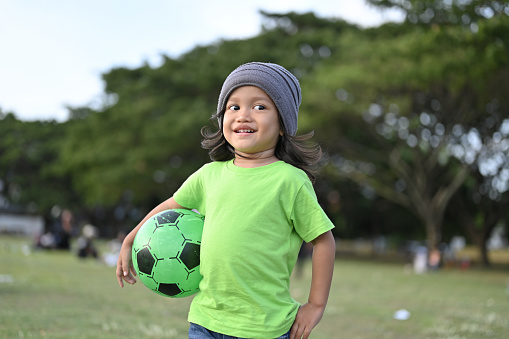 Asian toddler holding soccer ball in park