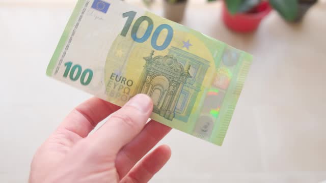 A man holds a 100 euro banknote in his hand close-up