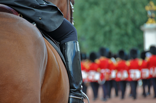 A captivating close-up of a leg and boot mounted on a horse outside Buckingham Palace in London, England, UK. The renowned Queen's Guard (now King's Guard) in their distinctive red jackets creates a striking backdrop.