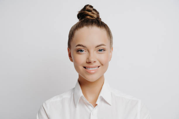 istock Happy female worker in white shirt, bright smile, excited about workplace developments, stands alone in front of light wall. 1545417655