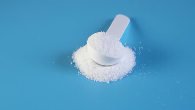 Pile of Aspartame powder with measuring spoon on blue background. Video 4K, Rotating. Sugar substitute, artificial sweetener. Food additive E951 used as sugar substitute in foods and beverages