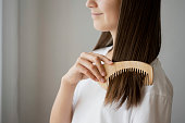 Beautiful young woman brushing her long brown hair with wooden comb.