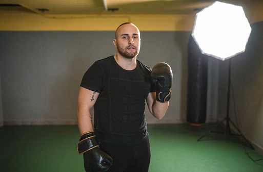 Portrait of a strong male boxer standing in the gym before boxing training and looking directly at the camera