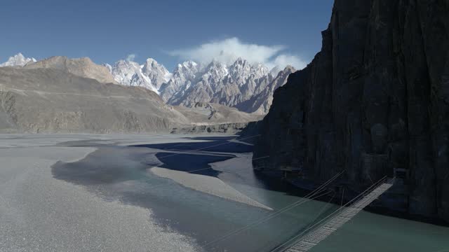 Hussaini Suspension bridge known as the most dangerous bridge in the world is only one of many precarious rope bridges in Northern Pakistan and distant Passu cones with indus river flowing below at Hussaini Village Hunza Valley, Gilgit Baltistan