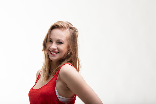 Strawberry-blonde woman in a fiery red dress. Smiling and laughing, she meets others' eyes confidently. Her half-length portrait is set against a white background with plenty of copyspace