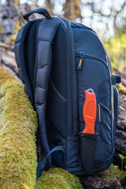 A red-handled knife on the side of a backpack in nature.