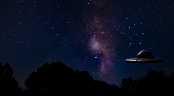 Bright Milky Way and stars with a UFO just above a dark forest