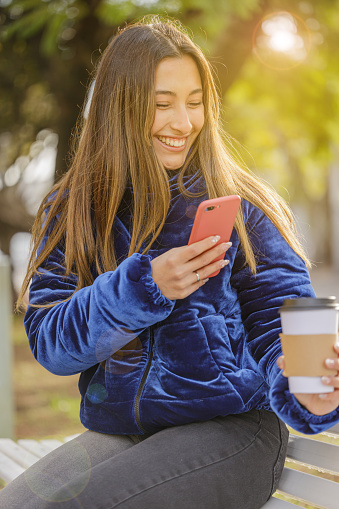 istock Latina girl taking a picture with her mobile phone of a disposable cup of coffee in a public park. 1545637812